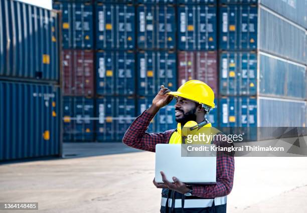 a worker is working at container shipyard for global business export and import using laptop. - african creative with laptop working outside stock-fotos und bilder