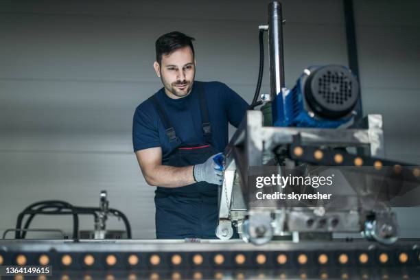 young worker working on a production line machine in a factory. - coveralls bildbanksfoton och bilder