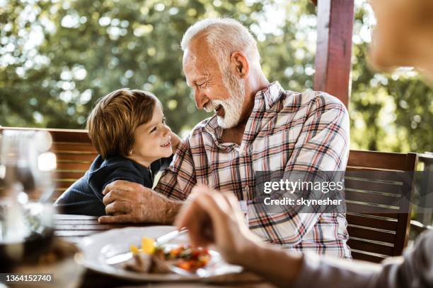 glücklicher senior mann spaßt mit seinem kleinen enkel während eines essens auf einem balkon. - balkon essen stock-fotos und bilder