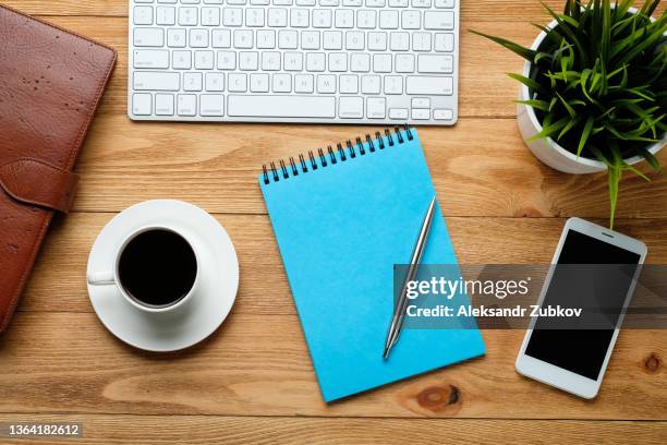 a mobile phone, a computer keyboard, a pen and notepad for notes, a coffee mug and a flower on a wooden table. subjects of work of a businessman or manager in the workplace. the concept of business, coffee break and breakfast. - coffee table from above stock-fotos und bilder