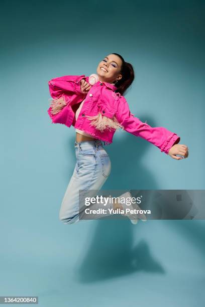 a girl in bright clothes with headphones and bright makeup jumps and smiles on a colored background in the studio - jumping girl stock pictures, royalty-free photos & images