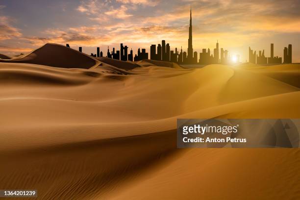 view of dubai from the desert with sand dunes at sunset - dubai desert stock-fotos und bilder