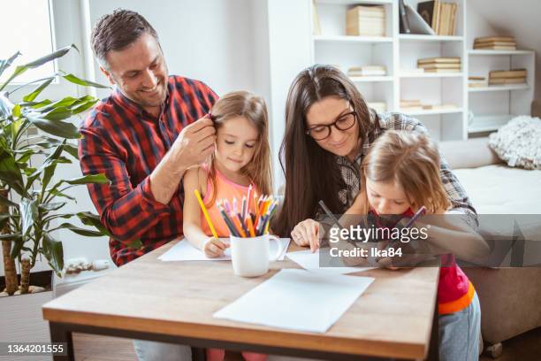 father and mother and their two young daughters having fun while doing drawing or writing exercise - report fun stock pictures, royalty-free photos & images