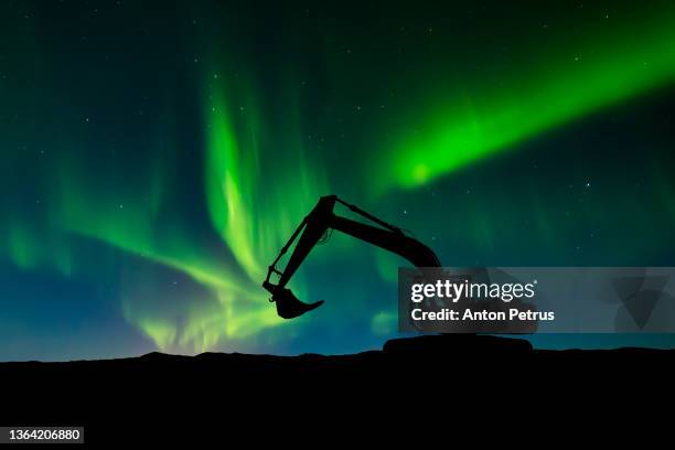 excavator at a construction site on a northern lights background. construction machinery - engineering earth stock pictures, royalty-free photos & images