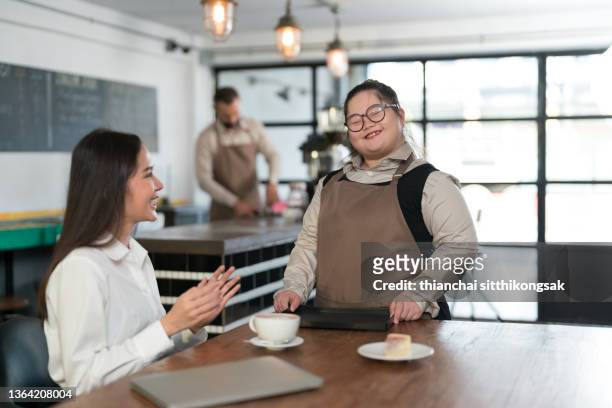 teenage girl with downs syndrome  serving coffee and cake in a café. - accessibilité aux personnes handicapées photos et images de collection