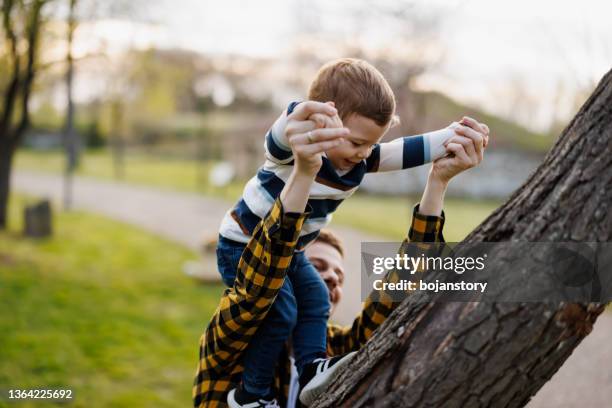 happy young father helping little son climb a tree - happy toddler stockfoto's en -beelden