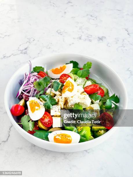 bowl of fresh salad (tomatoes, cucumber, spanish onion, olives, and avocado) with feta cheese and boiled eggs on white background - hard boiled eggs stock pictures, royalty-free photos & images