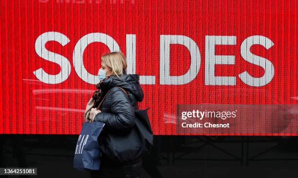 Woman wearing a protective face mask walks past a discount sign displayed on a store window on the first day of the winter sales on January 12, 2022...