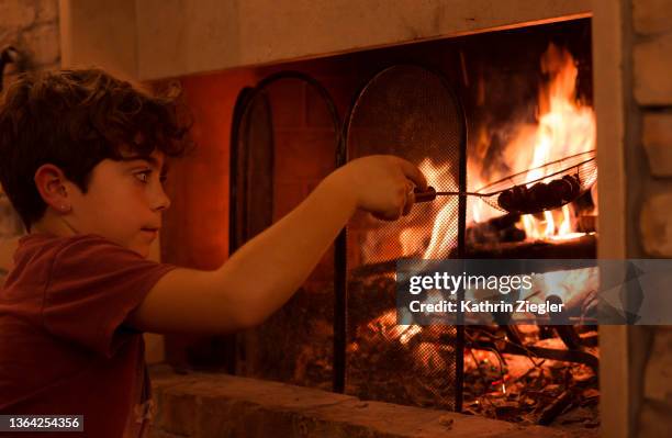 young boy roasting chestnuts at fireplace, using metal wire - camisa castanha imagens e fotografias de stock