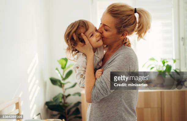 portrait of cheerful mother holding and kissing her daughter in the morning - good morning kiss images stock pictures, royalty-free photos & images