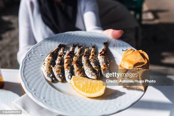 woman holding a plate of freshly cooked grilled sardines. - sardine photos et images de collection