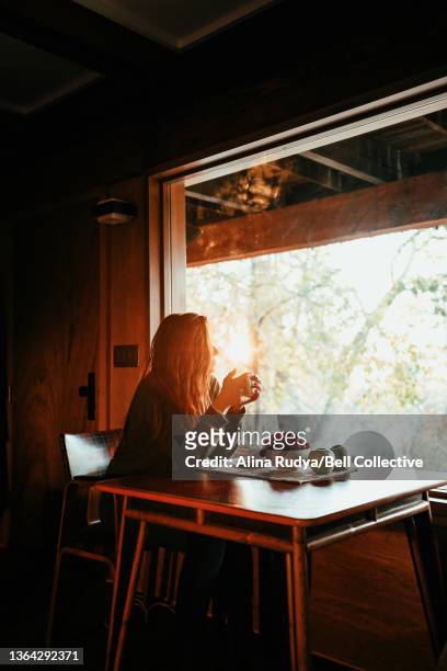 Woman drinking coffee in a sunlit wooden cabin