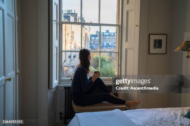 young woman enjoys a tea by window at home - bed side view stock pictures, royalty-free photos & images