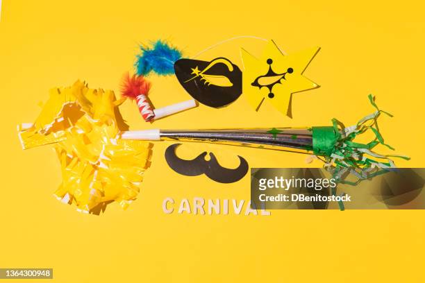 yellow and black cardboard mask with a blue feather, trumpet, sparkler and noisemaker with the wooden letters 'carnival', with hard shadow, on a yellow background. carnival and costume celebration concept. - blechblasinstrument stock-fotos und bilder