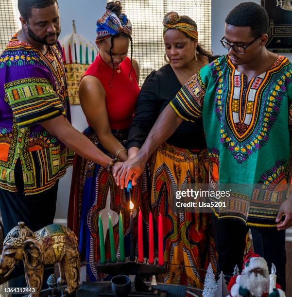 kwanzaa celebration, african american family lighting the kinara candle together at home in spirit of unity - kwanzaa celebration stock pictures, royalty-free photos & images