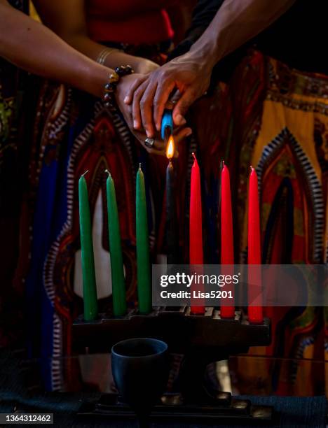 kwanzaa celebration, close up of family lighting the kinara candle in spirit of unity - kwanzaa stock pictures, royalty-free photos & images