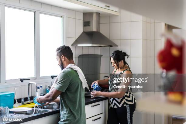 young man washes the dishes and a woman pours coconut water into the glass - domestic chores stock pictures, royalty-free photos & images