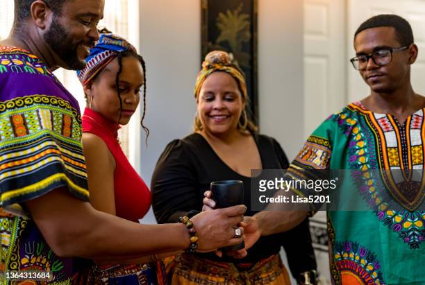 kwanzaa celebration, african american family holding the unity cup next to the kinara together at home - kwanzaa celebration stock pictures, royalty-free photos & images