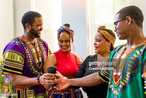 kwanzaa celebration, african american family holding the unity cup together at home with kinara - head tie stock pictures, royalty-free photos & images