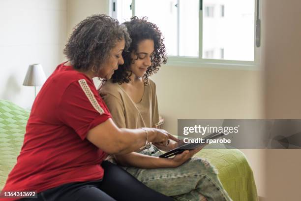 a joyful granddaughter shows the tablet to her grandmother - casa interior stock pictures, royalty-free photos & images