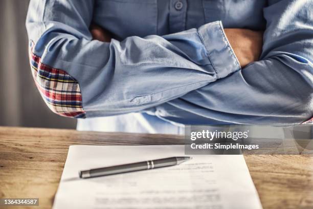 dissatisfied employee holds arms crossed over contract termination and a pen on the table in front of her. - cancelación fotografías e imágenes de stock