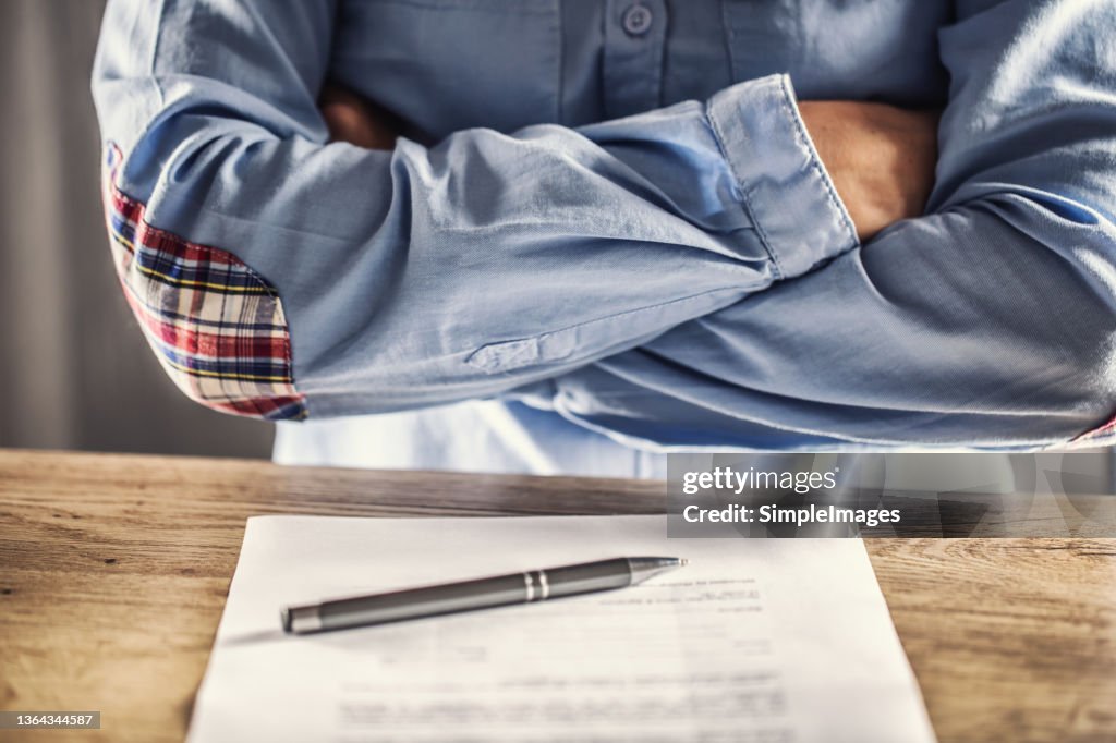 Dissatisfied employee holds arms crossed over contract termination and a pen on the table in front of her.