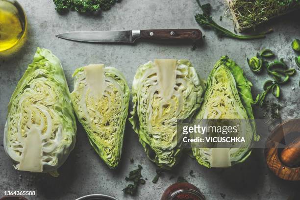 halves of white cabbage on grey concrete kitchen table with kitchen utensils and olive oil - cut cabbage stock pictures, royalty-free photos & images