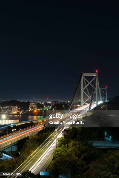 門司側から見た関門海峡をつなぐ関門橋と通過する自動車の軌跡 (kanmon bridge crossing the kanmon strait connecting kyushu and honshu islands) - 北九州市 fotografías e imágenes de stock