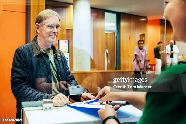 man talking to hospital receptionist before filling out forms - ersuchen stock-fotos und bilder