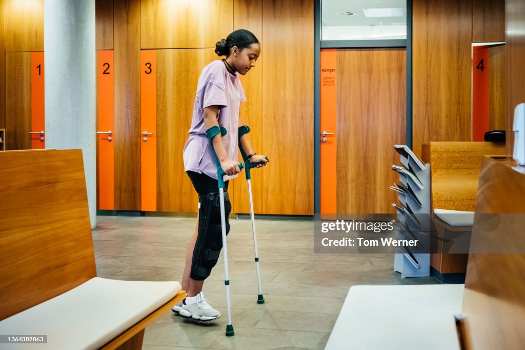 Injured Woman Walking With Crutches Through Hospital Reception