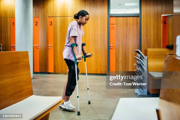 injured woman walking with crutches through hospital reception - crutch stock pictures, royalty-free photos & images