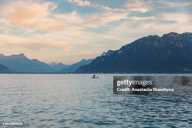 woman and man floating in the boat contemplating the scenic sunset above lake geneva and swiss alps mountains on background - geneva switzerland stock pictures, royalty-free photos & images