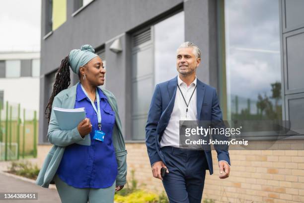 male and female school administrators walking on campus - administrative professionals stockfoto's en -beelden