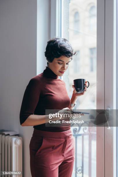 a beautiful businesswoman drinking her morning coffee and reading e-mails using her smartphone - turtleneck stockfoto's en -beelden