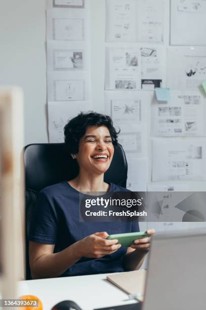 a latin-american woman being entertained at work by watching something funny on her mobile phone - relief emotion stock pictures, royalty-free photos & images