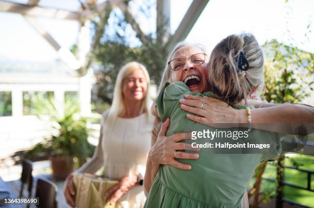 senior women hugging when congratulating during birthday celebration outdoors on patio at restaurant. - senior woman birthday stock pictures, royalty-free photos & images