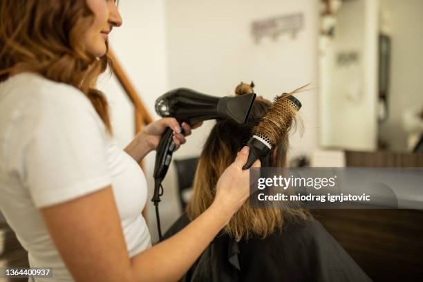 cabeleireira habilidosa, com secagem de secador de cabelo, seu cabelo cliente feminino - secador de cabelo - fotografias e filmes do acervo