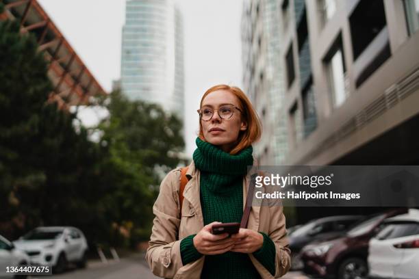 mid adult woman using smartphone and walking outdoors in city street on autumn day. - warme kleding stockfoto's en -beelden