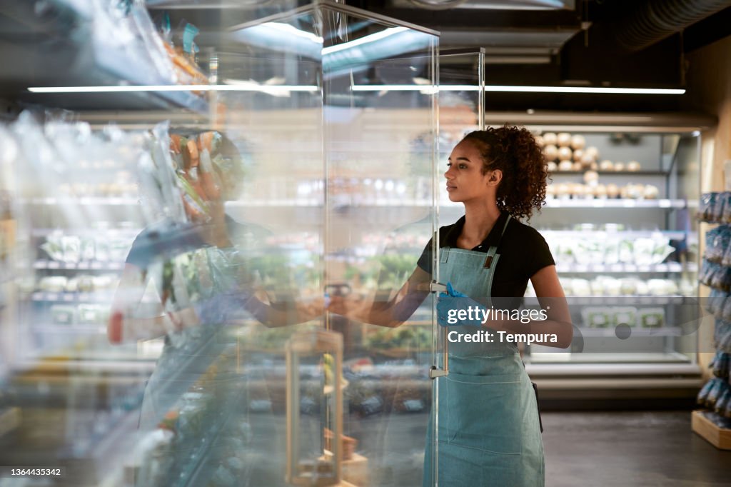A grocery store employee adjusting products in the fridge.