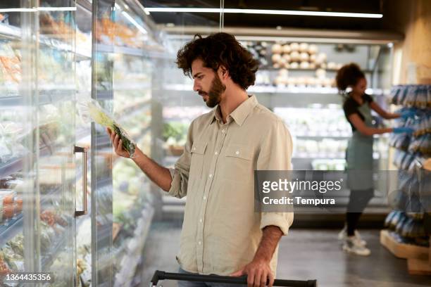 un hombre está eligiendo productos en la nevera de un supermercado. - pasillo objeto fabricado fotografías e imágenes de stock
