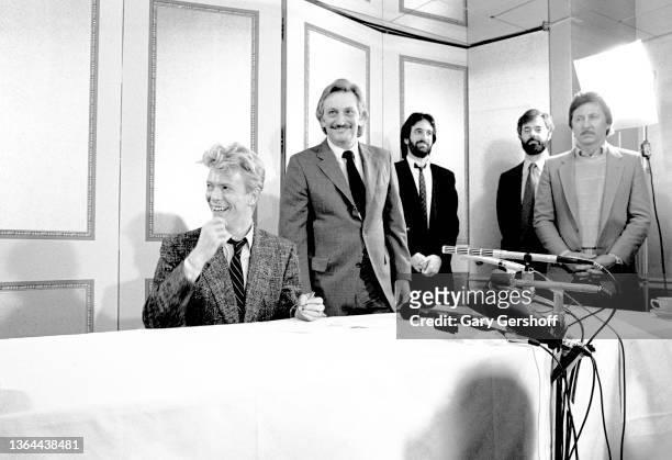 View of British Rock musician David Bowie as he signs a contract while unidentified EMI record executives watch at the Carlyle Hotel, New York, New...
