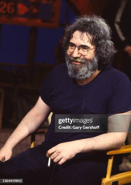 View of musician Jerry Garcia , a cigarette in his hand, as he sits in a director's chair during an interview on MTV at Teletronic Studios, New York,...