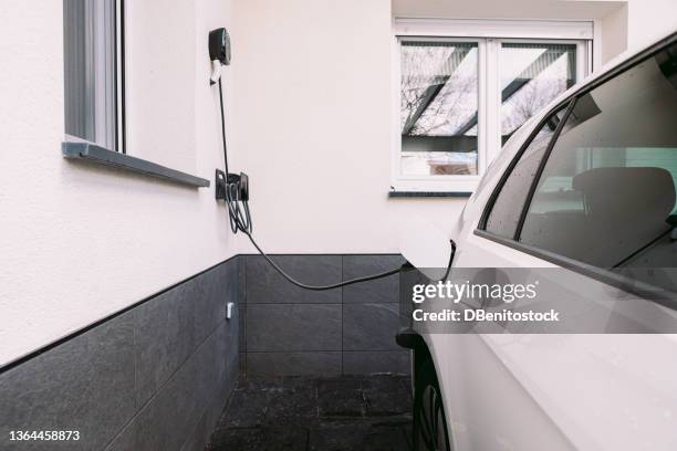 side view of an electric car with the cord plugged in charging the batteries in the garage outside a home. concept of electric car charging, renewable energy, sustainability and transport. - electric car home stock pictures, royalty-free photos & images