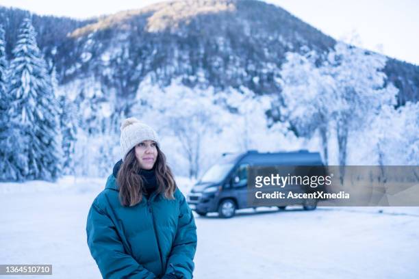 young woman leaves vehicle on a snowy lake below mountains - motor home winter stock pictures, royalty-free photos & images
