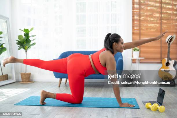 young woman doing yoga on exercise mat in her bedroom. healthy african woman practicing reclining back-bending yoga pose. - flat chested woman 個照片及圖片檔
