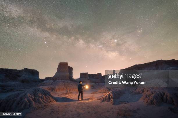 a male traveler stands under the stars in the wild with a lamp - explore imagens e fotografias de stock