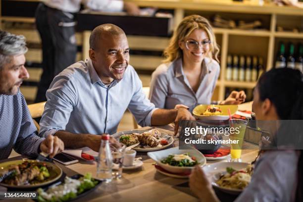 happy african american entrepreneur talking to his colleagues during lunch break in restaurant. - lunch break stockfoto's en -beelden