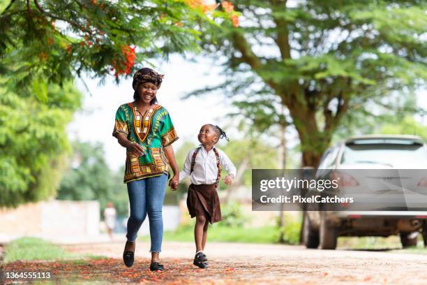 happy mother and schoolgirl walking down rural road to school - parent daughter school uniform stock pictures, royalty-free photos & images