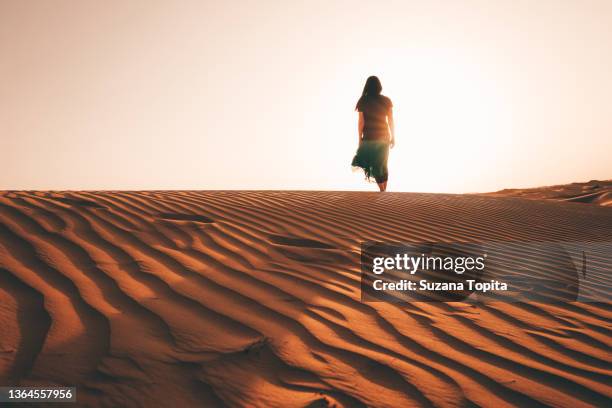 woman walking towards the sunset at golden hour on a sand dune - hot arab women stock-fotos und bilder