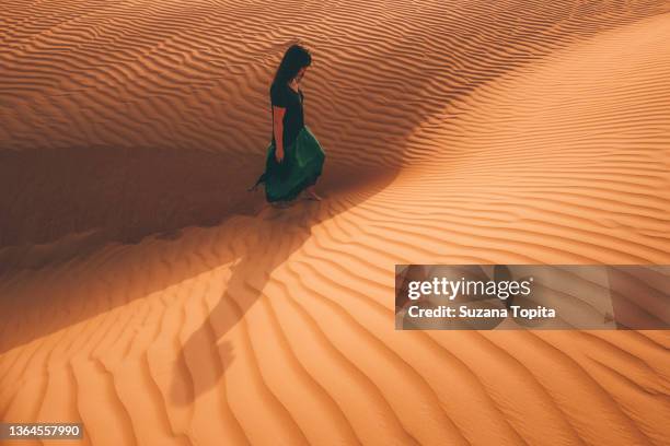 woman walking alone in the desert, surrounding by sand dunes - hot arabian women fotografías e imágenes de stock